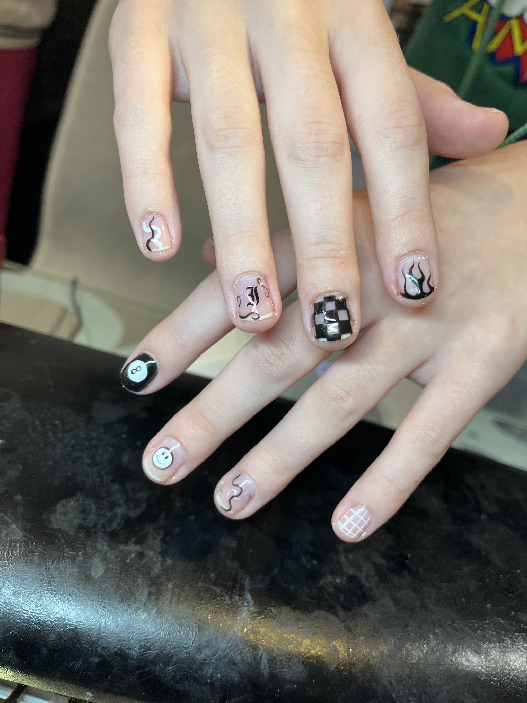 Korte nagels met zwart-witte mini designs: checkerboard, vlammen en een smiley